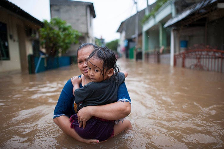 A woman carries a young child through a deeply flooded street